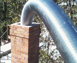 Stock photo of Chimney Relining - Advance Chimney New chimney liner being fed into top of brick chimney with scaffolding and trees in background