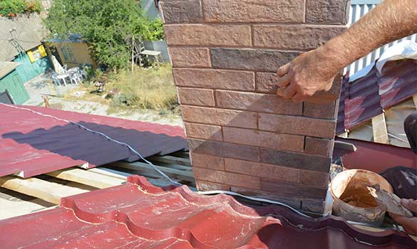 Tech repairing spalling on brick fireplace with tuckpointing on tile roof