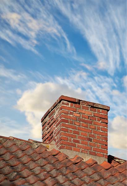 Brick chimney needing Masonry repair with tile roof and sweeping clouds in the background