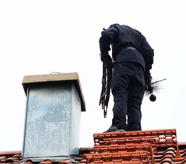 Chimney sweep on tiled roof inspecting chimney - Level 2 Inspection