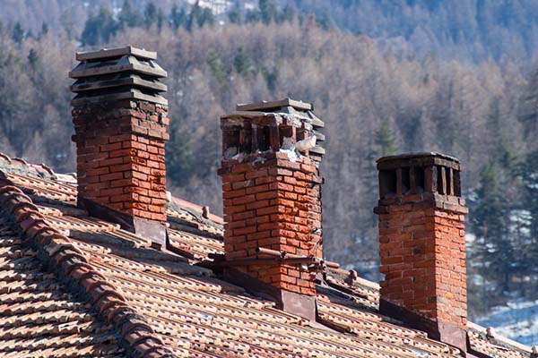 Three damaged chimneys on tile roof with snow and forest in the background