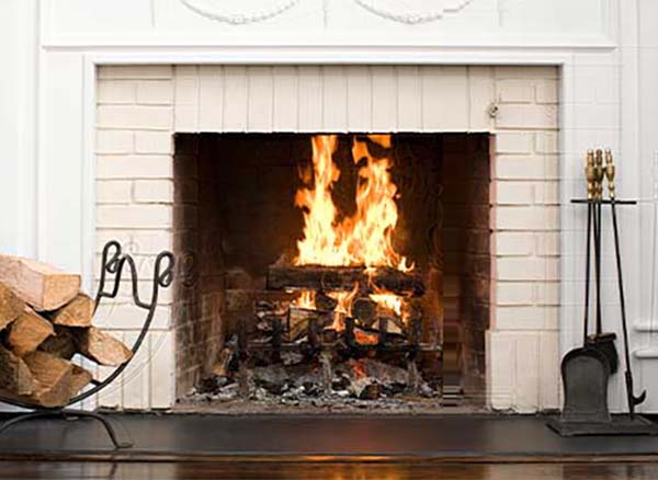 Fireplace with fire and new cream colored brick facing wood on one side and tools on the other