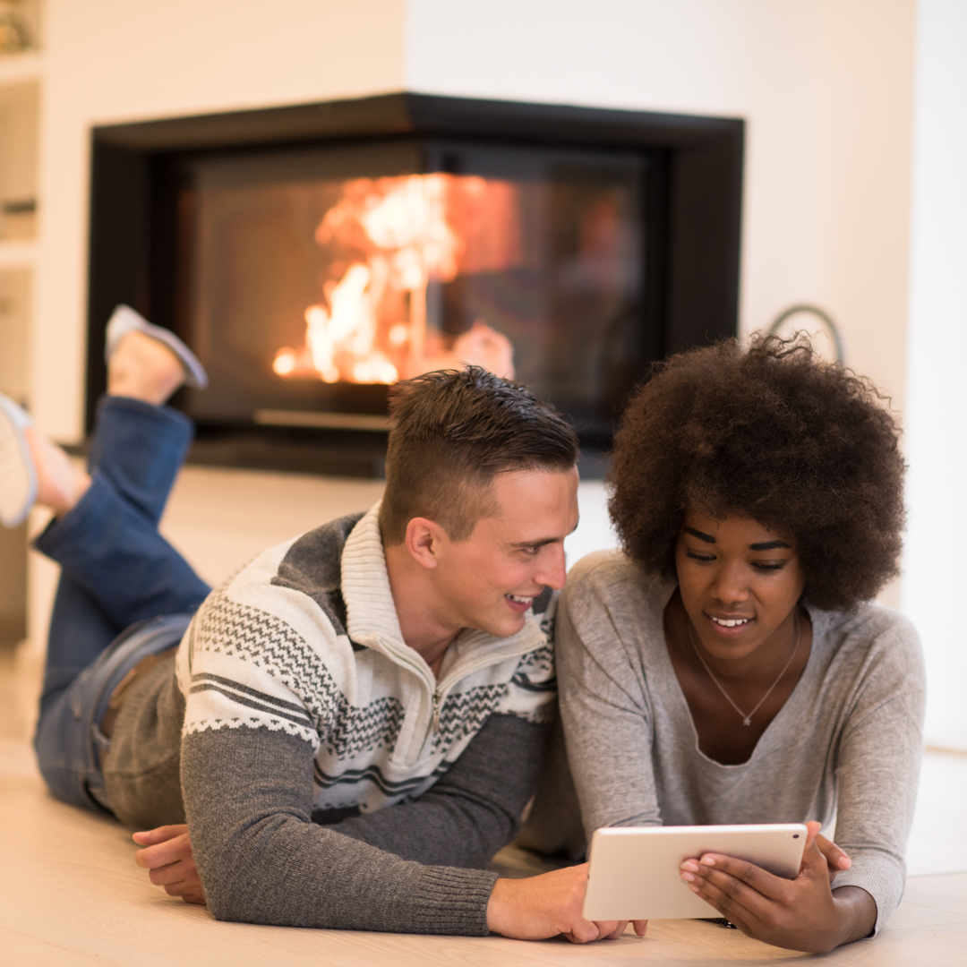 beautiful young multiethnic couple using tablet computer on the floor of their luxury home in front of fireplace at Valentine's Day